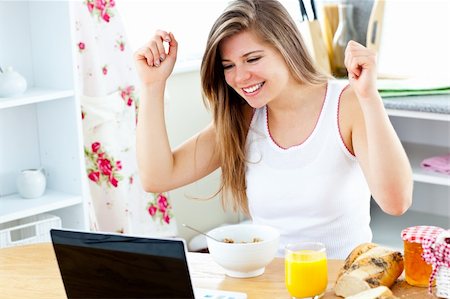 simsearch:400-04708507,k - Enthusiastic young woman looking at her laptop with arms up while having breakfast in the kitchen Stock Photo - Budget Royalty-Free & Subscription, Code: 400-04714565
