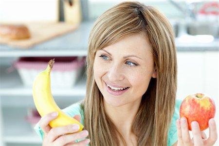 pretty women eating banana - Positive caucasian woman holing a bananan and an apple in the kitchen at home Photographie de stock - Aubaine LD & Abonnement, Code: 400-04716686