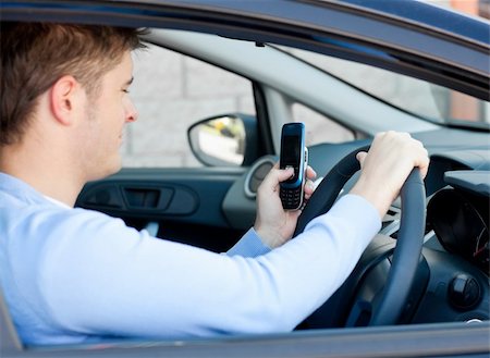 Cute young man sending a message with his mobile phone sitting in his car Stock Photo - Budget Royalty-Free & Subscription, Code: 400-04711368