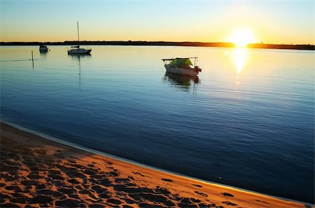 simsearch:400-04978777,k - Sun streams over small boats in a still lagoon at dawn. Photographie de stock - Aubaine LD & Abonnement, Code: 400-04711390