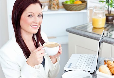 simsearch:400-04209411,k - Glowing businesswoman drinking coffee smiling at the camera sitting in the kitchen at home Fotografie stock - Microstock e Abbonamento, Codice: 400-04724735