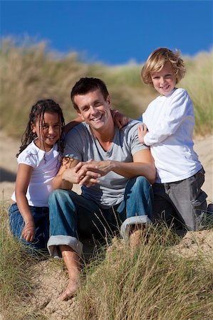 simsearch:400-04235471,k - A man mixed race girl and young boy, father, son and daughter, sitting down and having fun in the sand dunes of a sunny beach Stock Photo - Budget Royalty-Free & Subscription, Code: 400-04738569