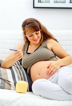 simsearch:400-04859723,k - Smiling beautiful pregnant woman sitting on sofa and knitting for her baby. Fotografie stock - Microstock e Abbonamento, Codice: 400-04747899
