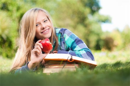 beautiful young student girl lying on grass with red apple in her hand and books under her hands, looking into the camera and smiling Stock Photo - Budget Royalty-Free & Subscription, Code: 400-04743967