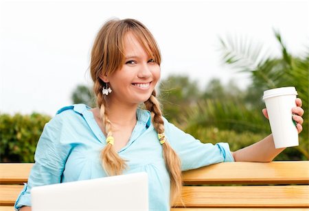 beautiful young student girl sitting on bench with laptop in campus park, smiling and looking into the camera. Holding cup of coffee in her  hand Fotografie stock - Microstock e Abbonamento, Codice: 400-04743978