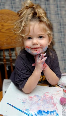 Adorable little girl poses besides her masterpiece.  She has paint smeared on her face and hands. Foto de stock - Royalty-Free Super Valor e Assinatura, Número: 400-04757898