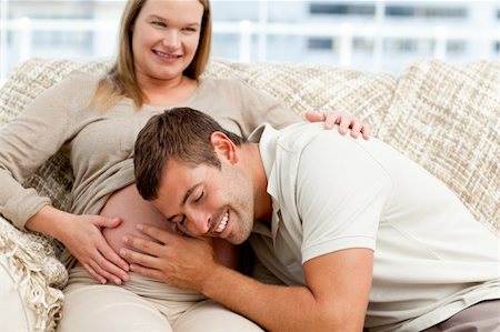 simsearch:400-07322828,k - Attentive future dad listening to the belly of his wife sitting on the sofa in the living room Fotografie stock - Microstock e Abbonamento, Codice: 400-04767795