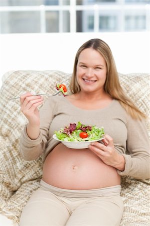 simsearch:400-04767824,k - Cheerful pregnant woman eating vegetables in the living room Foto de stock - Royalty-Free Super Valor e Assinatura, Número: 400-04767824