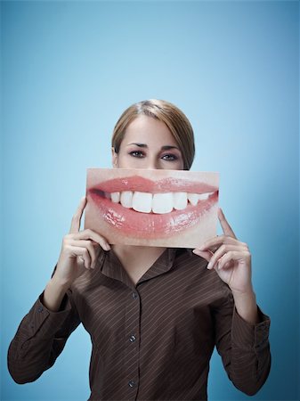 mid adult business woman holding photo of toothy smile on blue background. Vertical shape, front view, waist up, copy space Stock Photo - Budget Royalty-Free & Subscription, Code: 400-04768679