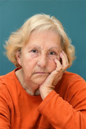 Real senior woman sulking, looking at camera. Much facial details like brown aged spots, wrinkles, no make-up, great color contrast of blue wall and orange shirt. Fotografie stock - Microstock e Abbonamento, Codice: 400-04760475