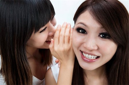 simsearch:400-05138908,k - Two happy asian friends talking secretly over white background. Photographie de stock - Aubaine LD & Abonnement, Code: 400-04775926