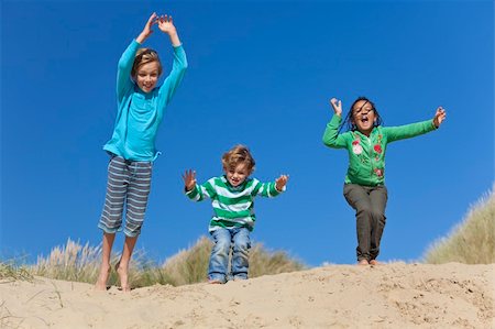 Three children, two blond boys and a mixed race little girl, having fun arms raised and jumping in the dunes of a sandy beach Stock Photo - Budget Royalty-Free & Subscription, Code: 400-04787531