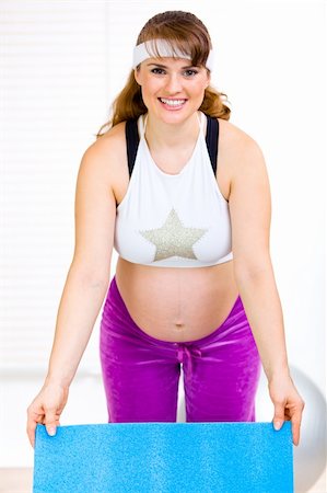 Smiling beautiful pregnant woman holding exercise mat in hands at living room Stock Photo - Budget Royalty-Free & Subscription, Code: 400-04793347