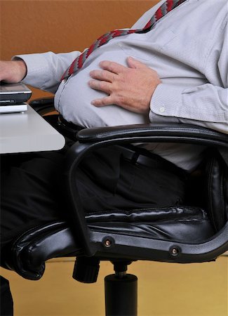 Middle aged man sitting in his office holding his large stomach while working at his desk.  Sedintary men with heavy mid sections are more at risk for diabetes, heart attacks and strokes. Stock Photo - Budget Royalty-Free & Subscription, Code: 400-04837162