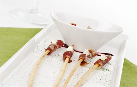 salzstange - Thin ham slices wrapped around thin bread sticks and served on a long plate on a green place mat with a wine glass in the background (Selective Focus) Stockbilder - Microstock & Abonnement, Bildnummer: 400-04840200