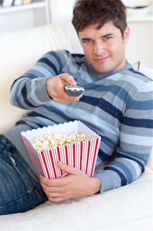 Relaxed young man eating popcorn and holding a remote lying on the sofa at home Stock Photo - Budget Royalty-Free & Subscription, Code: 400-04841242