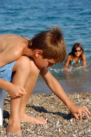 little boy playing with rocks on pebble beach by blue sea Foto de stock - Super Valor sin royalties y Suscripción, Código: 400-04843269