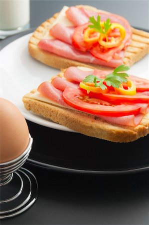 Fresh pork tenderloin sandwiches with cheese, tomato and pepper arranged in ceramic plates in the company of soft-boiled egg placed in a special metal stand and glass of milk Stock Photo - Budget Royalty-Free & Subscription, Code: 400-04855434