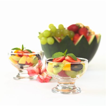 simsearch:400-04859746,k - Fresh fruit salad with strawberry, kiwi, mango and grapes in glass bowl garnished with mint leaf with Inca Lily and a watermelon bowl full of fruits in the back (Selective Focus, Focus on the mint leaf in the first bowl) Foto de stock - Super Valor sin royalties y Suscripción, Código: 400-04859738
