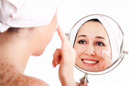 simsearch:400-03935575,k - Beautiful happy smiling woman face applying exfoliating cream as anti-aging skincare treatment while looking at mirror, isolated. Stock Photo - Budget Royalty-Free & Subscription, Code: 400-04853124