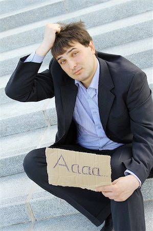 simsearch:400-08496169,k - Young businessman sitting on the stairs of the building in hand bumga cardboard with the text "aaaa.." with his other hand holding his head Stock Photo - Budget Royalty-Free & Subscription, Code: 400-04867607