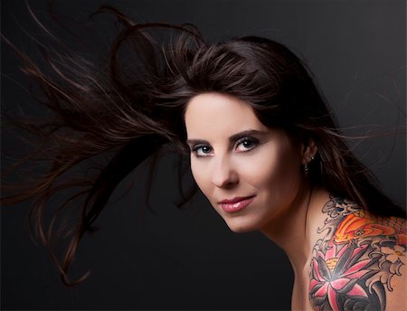 Portrait of a lovely woman with a tatto on the shoulder against a grey background and spread hair Stock Photo - Budget Royalty-Free & Subscription, Code: 400-04860015
