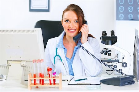 simsearch:400-04925813,k - Smiling medical doctor woman sitting at office table and talking on phone Stock Photo - Budget Royalty-Free & Subscription, Code: 400-04874960