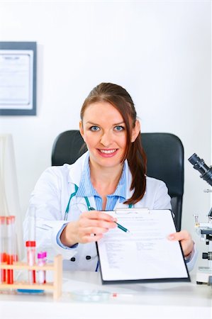 simsearch:400-04390415,k - Smiling medical doctor woman sitting at office table with document and pen for signing Stock Photo - Budget Royalty-Free & Subscription, Code: 400-04874963