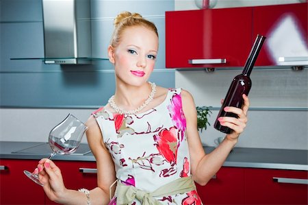 young beautiful blonde girl wearing white and pink dress holding glass and bottle with wine in interior of modern red kitchen in expectation of party Stockbilder - Microstock & Abonnement, Bildnummer: 400-04877729