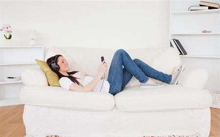 simsearch:400-04418452,k - Attractive red-haired female listening to music with headphones while lying on a sofa in the living room Photographie de stock - Aubaine LD & Abonnement, Code: 400-04878719