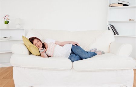 Beautiful red-haired female watching tv while lying on a sofa in the living room Stock Photo - Budget Royalty-Free & Subscription, Code: 400-04878763