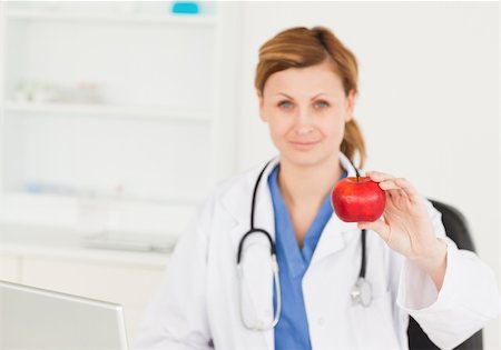 photo of desk with apple laptop - Young female doctor showing a red apple in her surgery Stock Photo - Budget Royalty-Free & Subscription, Code: 400-04871346