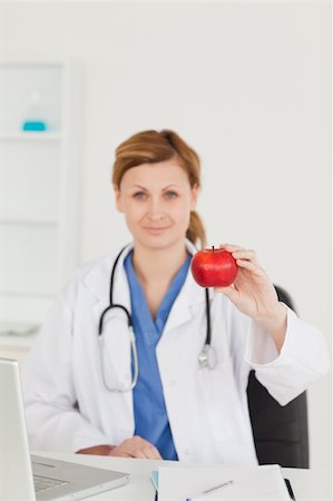 photo of desk with apple laptop - Cute female doctor showing a red apple to the camera in her surgery Stock Photo - Budget Royalty-Free & Subscription, Code: 400-04871347