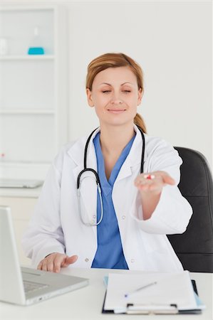 simsearch:400-04191693,k - Attractive female doctor showing pills to the camera while sitting in her office Stock Photo - Budget Royalty-Free & Subscription, Code: 400-04871353