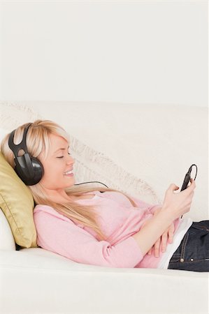 simsearch:400-04418454,k - Good looking woman listening to music on her headphones while lying on a sofa in the living room Stockbilder - Microstock & Abonnement, Bildnummer: 400-04871472