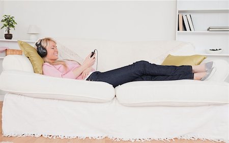 simsearch:400-04418454,k - Pretty woman listening to music on her headphones while lying on a sofa in the living room Stockbilder - Microstock & Abonnement, Bildnummer: 400-04871513