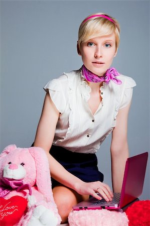 Portrait of beautiful blond girl wearing short skirt and white shoes near pink rabbit working with pink laptop on blue background Stockbilder - Microstock & Abonnement, Bildnummer: 400-04872515