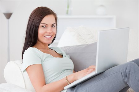 Beautiful woman typing on her laptop while sitting on her sofa while looking at the camera Stock Photo - Budget Royalty-Free & Subscription, Code: 400-04884031