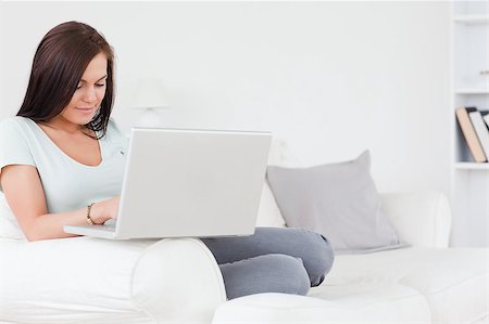 Young brunette sitting on a sofa using a laptop looking away from the camera Stock Photo - Budget Royalty-Free & Subscription, Code: 400-04884269