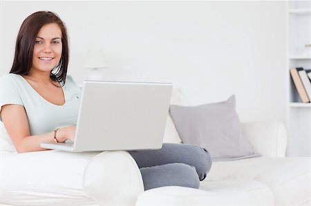 simsearch:400-04999709,k - Close up of a charming brunette sitting on a sofa using a laptop looking at the camera Photographie de stock - Aubaine LD & Abonnement, Code: 400-04884270