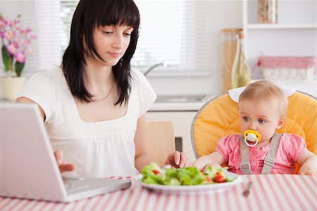 family eating computer - Gorgeous brunette woman eating a salad next to her baby while relaxing with her laptop in the kitchen Stock Photo - Budget Royalty-Free & Subscription, Code: 400-04884547