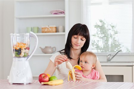 Attractive brunette woman pealing a banana while holding her baby on her knees in the kitchen Stock Photo - Budget Royalty-Free & Subscription, Code: 400-04884564