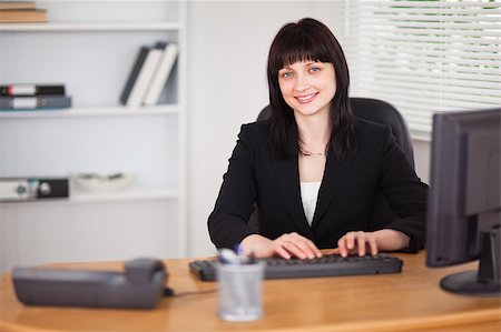 simsearch:400-04894274,k - Pretty brunette woman working on a computer while sitting at a desk in the office Stock Photo - Budget Royalty-Free & Subscription, Code: 400-04884576