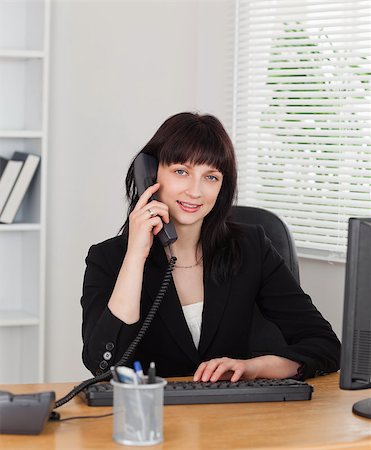simsearch:400-04894274,k - Good looking brunette woman on the phone while working on a computer in the office Stock Photo - Budget Royalty-Free & Subscription, Code: 400-04884580