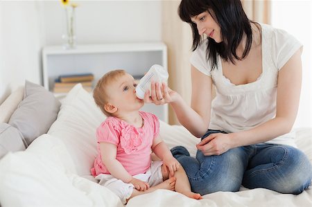 Charming brunette female bottle-feeding her baby on a bed in her appartment Stock Photo - Budget Royalty-Free & Subscription, Code: 400-04884635