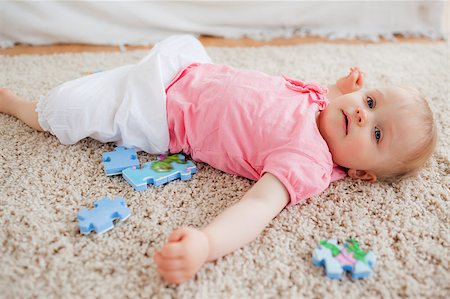 Cute blond baby playing with puzzle pieces while lying on a carpet in the living room Stock Photo - Budget Royalty-Free & Subscription, Code: 400-04884666