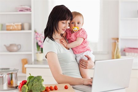 simsearch:400-04712944,k - Charming woman holding her baby in her arms while standing in the kitchen Stock Photo - Budget Royalty-Free & Subscription, Code: 400-04884708