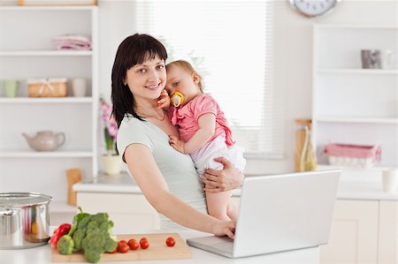simsearch:400-04712944,k - Lovely woman holding her baby in her arms while standing in the kitchen Stock Photo - Budget Royalty-Free & Subscription, Code: 400-04884709