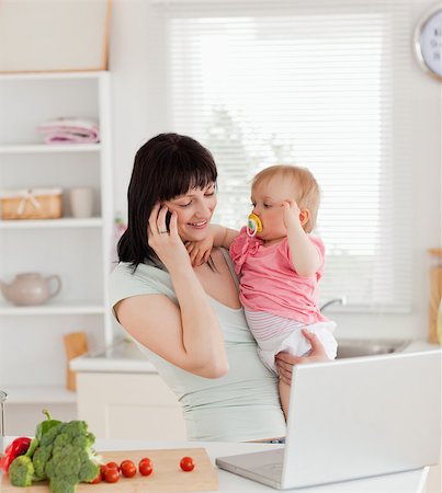 simsearch:400-04712944,k - Attractive brunette woman on the phone while holding her baby in her arms in the kitchen Stock Photo - Budget Royalty-Free & Subscription, Code: 400-04884715