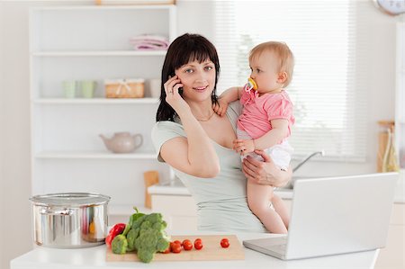 simsearch:400-04712944,k - Charming brunette woman on the phone while holding her baby in her arms in the kitchen Stock Photo - Budget Royalty-Free & Subscription, Code: 400-04884717